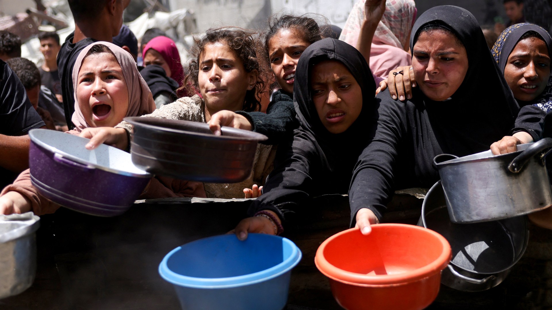 Displaced Palestinians gather to collect portions of cooked food at a charity distribution point in Gaza.